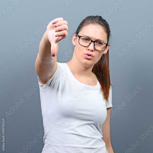Portrait of a woman showing thumb down as disapproval against gr