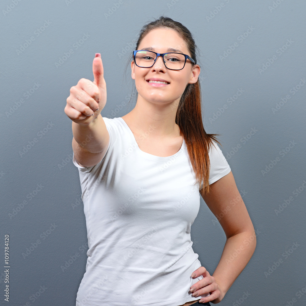 Portrait of happy woman holding thumbs up against gray backgroun Portrait of happy woman holding thumbs up against gray backgroun