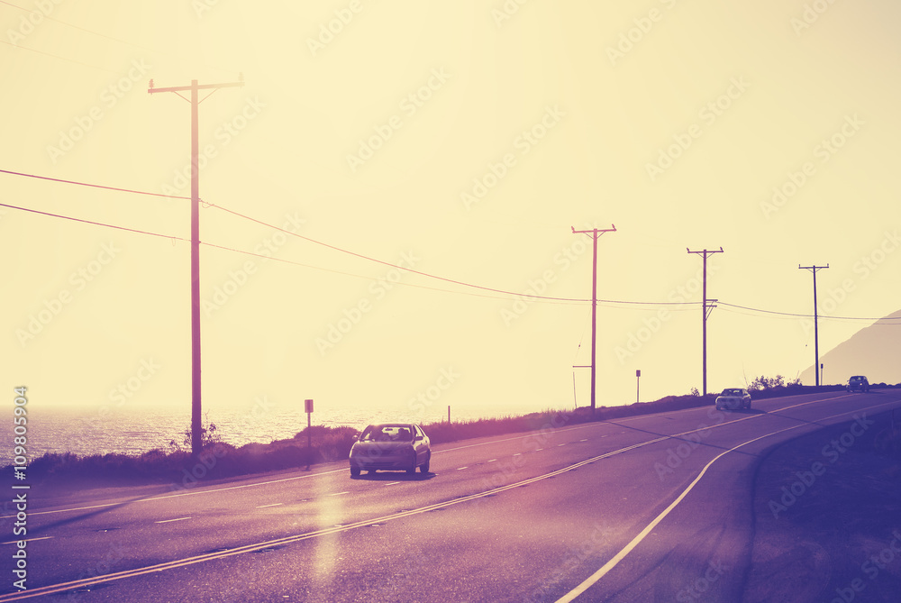 Vintage toned ocean road against sun with flare effect, travel concept.