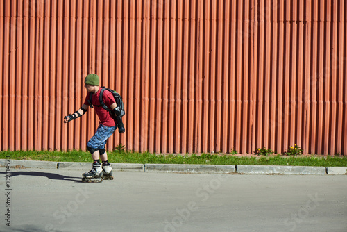 Guy rides on roller skates on an asphalt track against the red wall