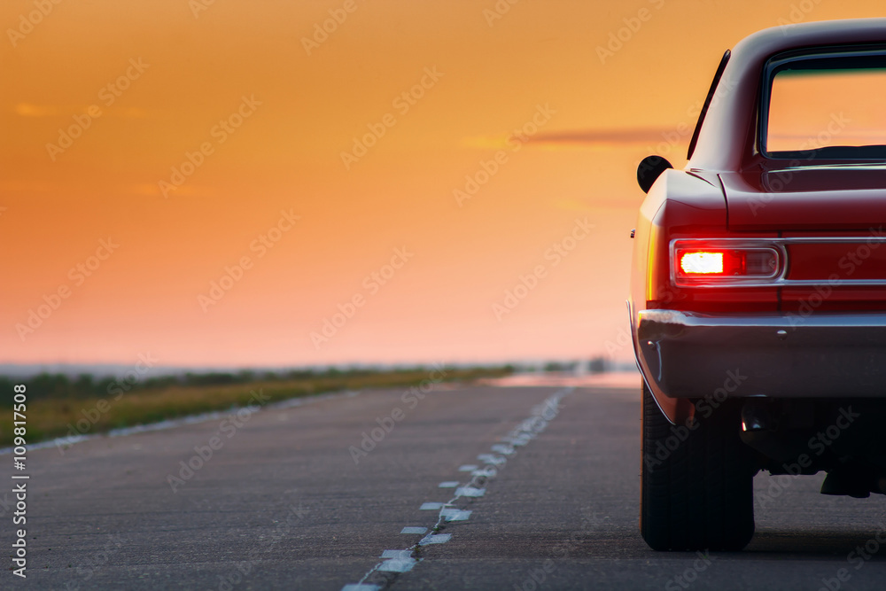 Naklejka premium Retro red car standing on asphalt road at sunset
