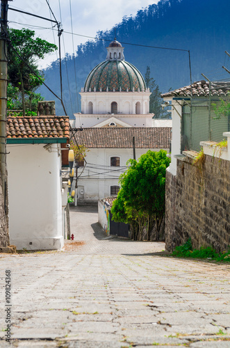 Charming village located outside Quito Ecuador with bridgestone road leading down to dome tower of spanish colonial building photo