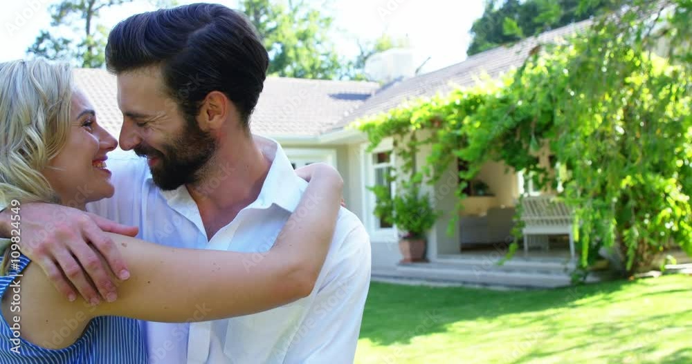 Cute couple smiling and holding each other in front of a house Cute couple smiling and holding each other in front of a house