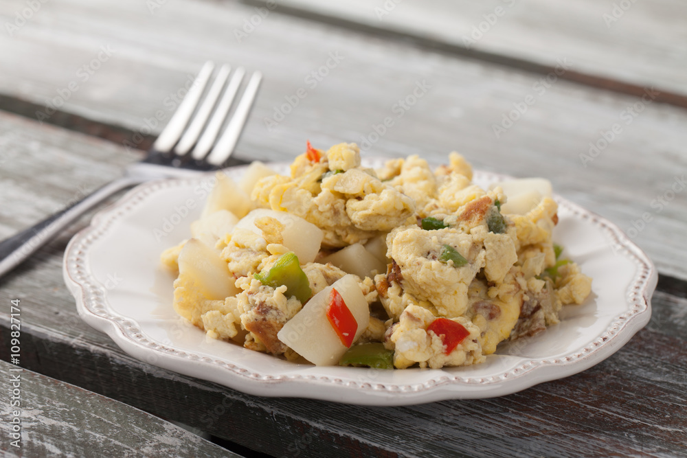 Scrambled eggs with Anaheim chilies, boiled potatoes, green peppers, and onions on a weathered barn wood table