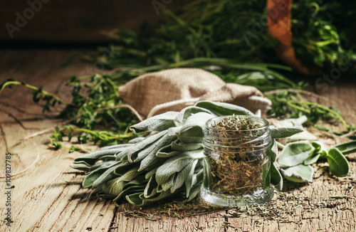 Dried sage in a glass jar, fresh sage on the vintage wooden tabl photo
