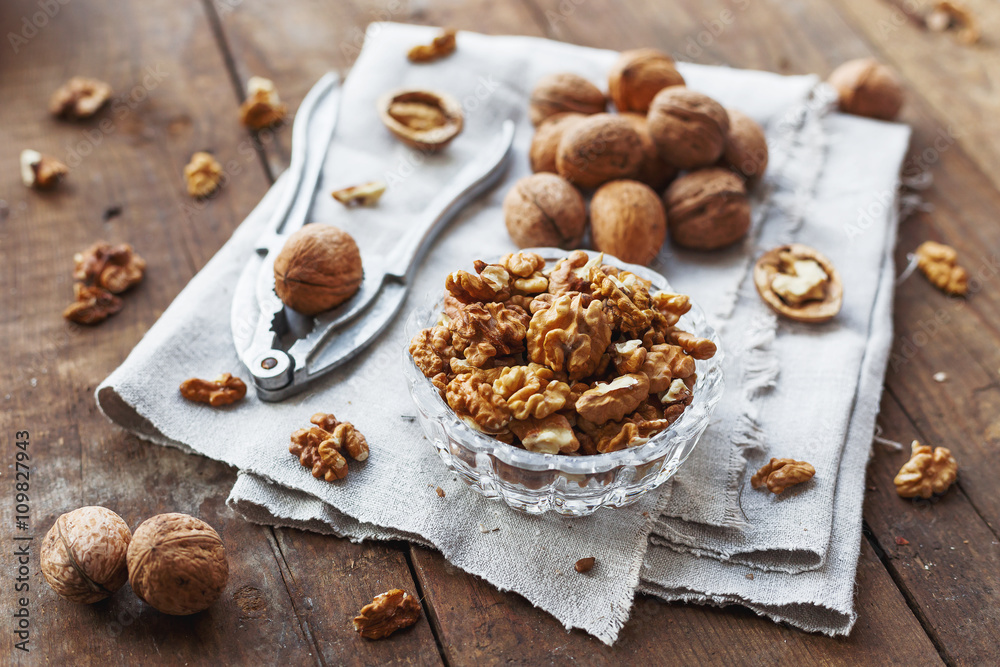 Fototapeta premium Glass bowl with walnuts on rustic homespun napkin. Healthy snack on old wooden background.