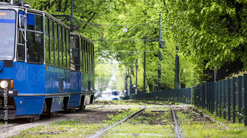 Blue tram driving through green alley in European city of Krakow, Poland