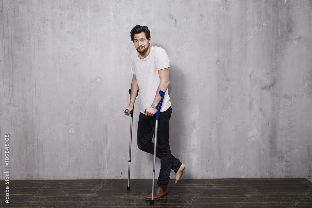 Young man with injury on crutches in studio, portrait Young man with injury on crutches in studio, portrait