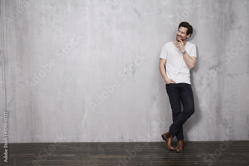 Thoughtful young man standing against wall, smiling © sanneberg