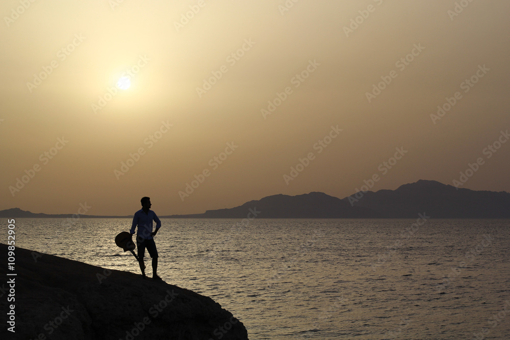 lonely figure of a man on a cliff by the sea with guitar
