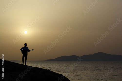 lonely figure of a man on a cliff by the sea with guitar