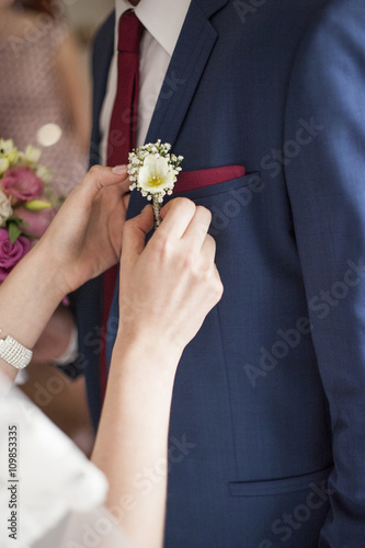 Przypinanie butonierki ślubnej z kwiatów do garnituru pana młodego