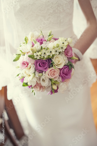 Wiązanka ślubna z kolorowych kwiatów panny młodej na tle sukni ślubnej