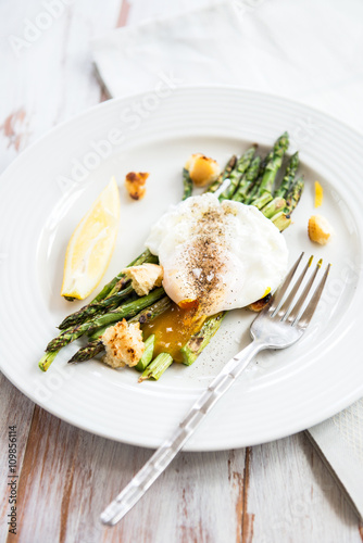 Green Griddled Asparagus with Poached Egg, Lemon and Sourdough Crumbs on a Plate, Light Background