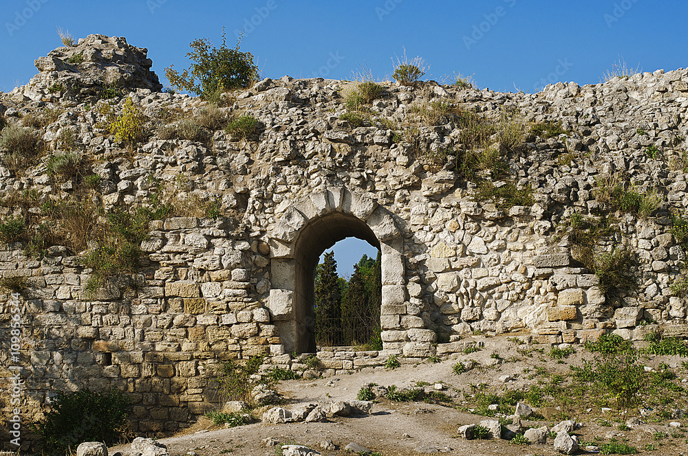 Ruins of ancient Greek sandstone wall with an arch doorway