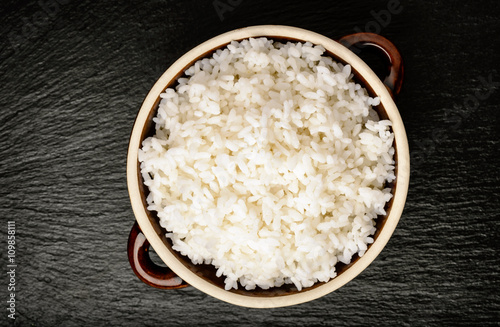 Boiled white rice in ceramic pot on black background.