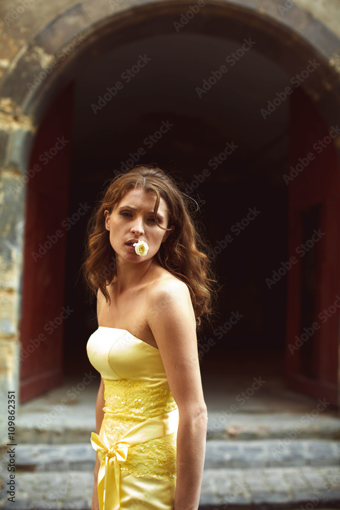 Naklejka premium Woman in yellow dress with rose in her mouth stands in the front