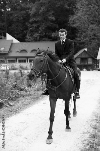 Man in balck suit rides a horse along the road