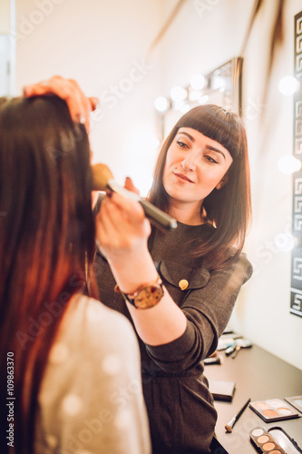 Professional expert,makeup artist prepares very beautiful,young,well-known,glamorous,stunning model for filming shooting for cover of fashion magazine VOGUE,does make-up,makes up lips,art,eyes,white.