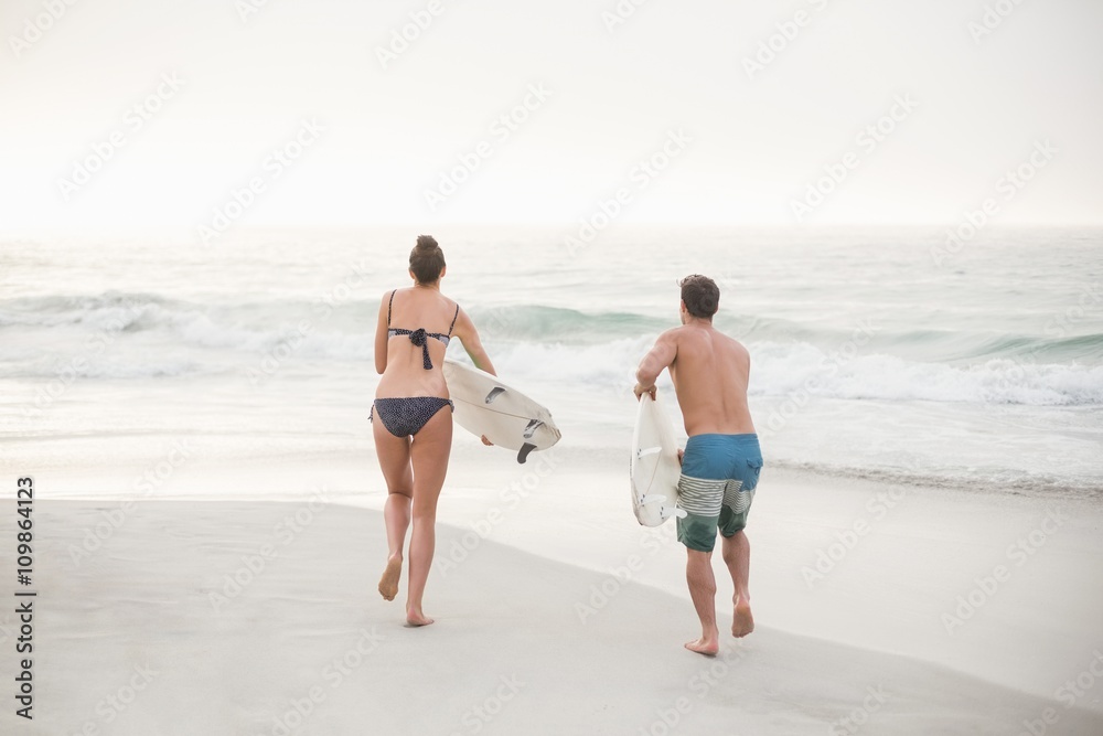 Rear view of couple running with a surfboard on the beach Rear view of couple running with a surfboard on the beach