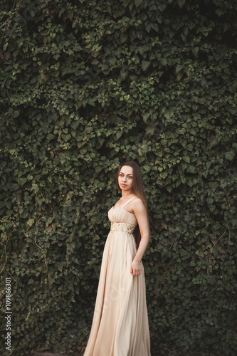 Beautiful girl, model near the wall of leaves and bushes in park