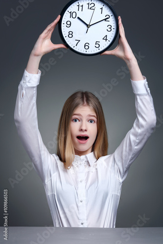 Surprised blondgirl with huge alarm clock on light background. photo