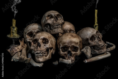 Pile of skulls and bones with two candles and smoke on black background. Genocides concept still life style.