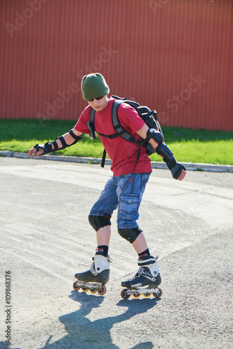 The guy is going backwards on roller skates on an asphalt track against the red wall