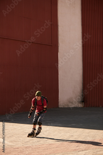Guy rides on roller skates on the pavement against the red wall © amixstudio