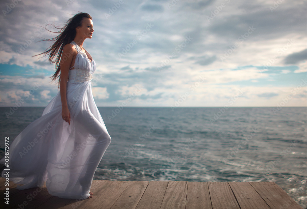 Gorgeous woman in white dress standing at pier close to cliffs. Gorgeous woman in white dress standing at pier close to cliffs.