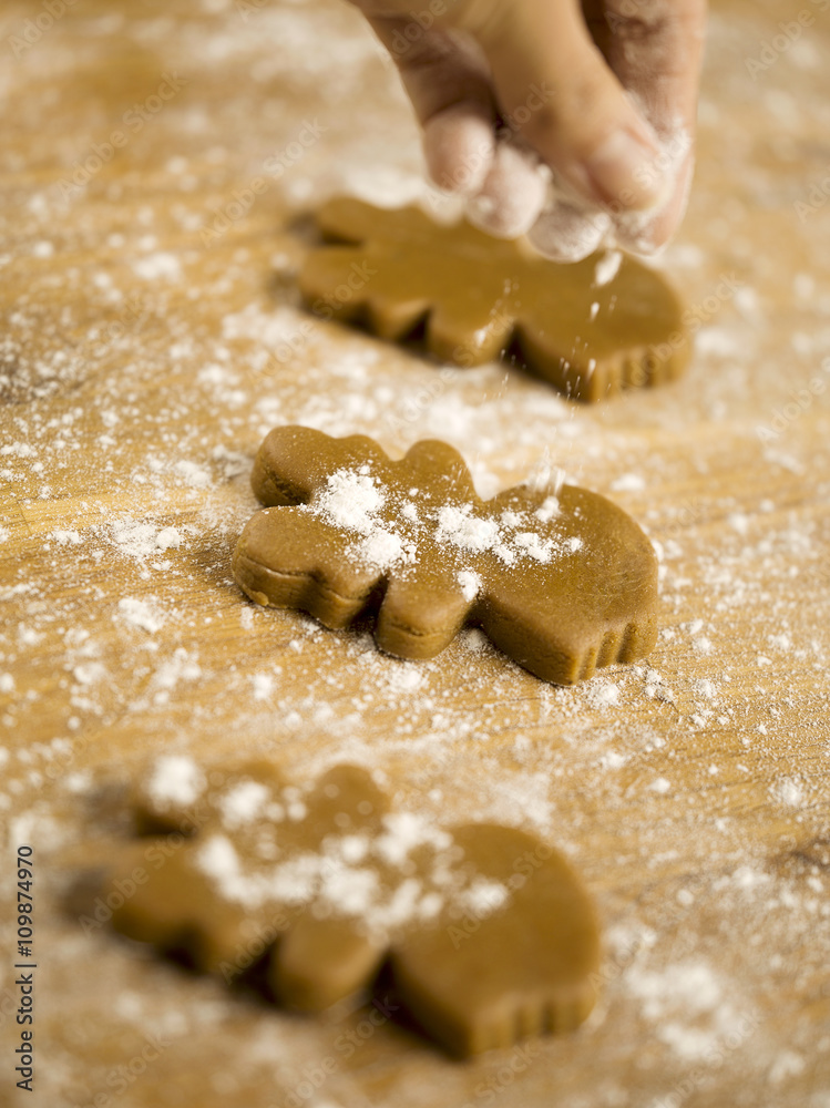 hand sprinkling flour on gingerbread cookie. hand sprinkling flour on gingerbread cookie.