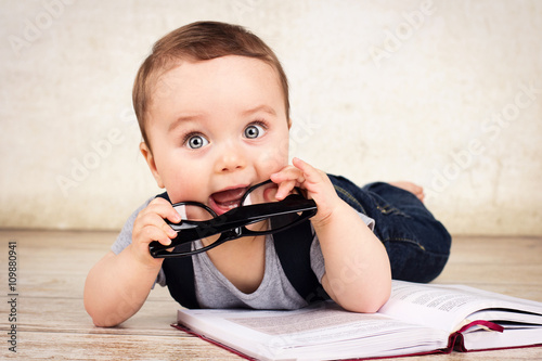 Lovely little baby boy with glasses reading a book