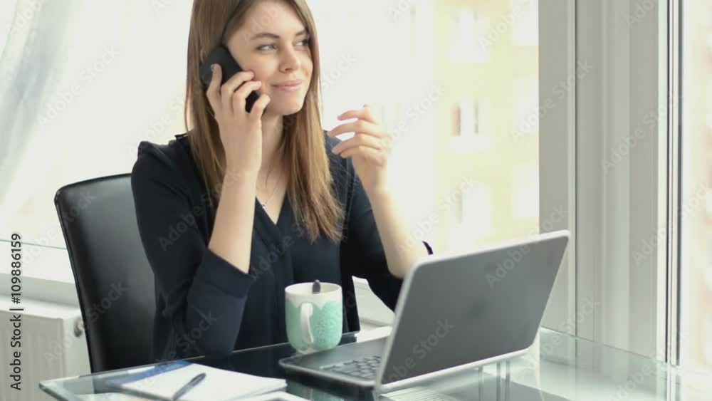 Business woman speaks on the phone in her office, typing on laptop Business woman speaks on the phone in her office, typing on laptop