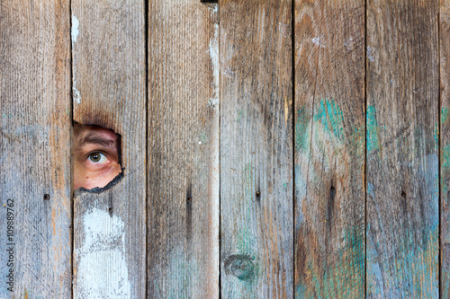 the eyes of a man spying through a hole in an old wooden fence. with space for posting information photo