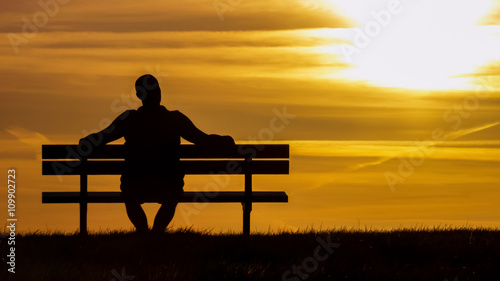 Silhouette man sitting on a bench looking up at the sunset 