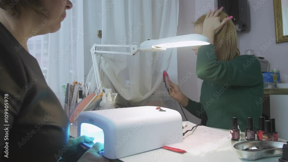 Manicurist choose color of lacquer with client in beauty saloon. Hands in ultraviolet lamp. Shellac cover. Medium shot Manicurist choose color of lacquer with client in beauty saloon. Hands in ultraviolet lamp. Shellac cover. Medium shot
