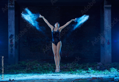 Young woman jumping in blue powder cloud