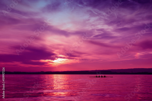 Rowers in a rowing boat silhouette on sunset background in lake,