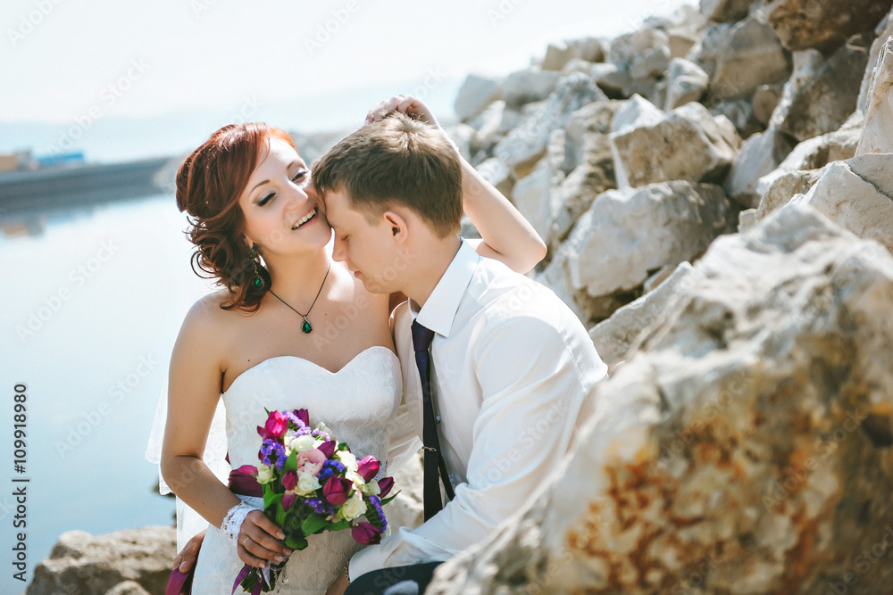 Happy smiling young bride and groom, walking on the rocks, beautiful sky, water. The couple love each other. Happy smiling young bride and groom, walking on the rocks, beautiful sky, water. The couple love each other.