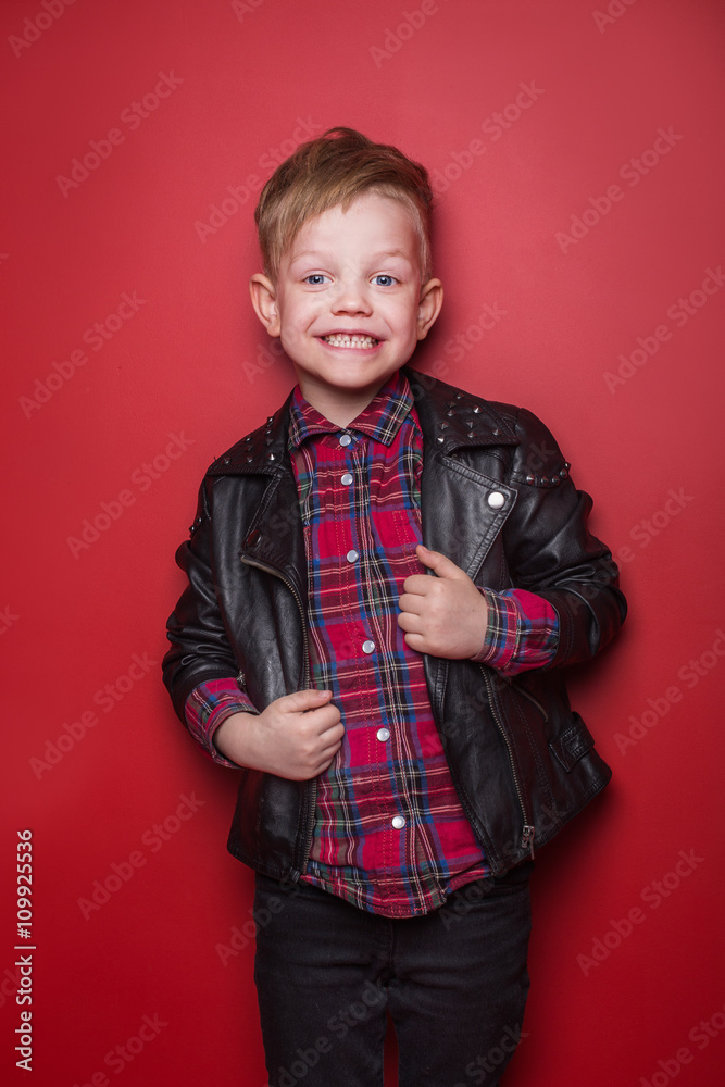 Fashion little boy wearing a leather jacket. Studio portrait over red background Fashion little boy wearing a leather jacket. Studio portrait over red background