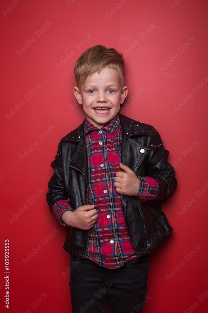 Fashion little boy wearing a leather jacket. Studio portrait over red background Fashion little boy wearing a leather jacket. Studio portrait over red background