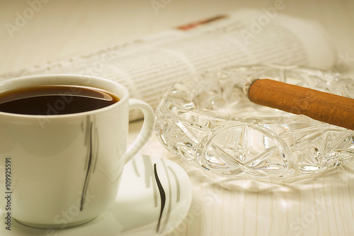 Lit cigar, coffee and newspaper