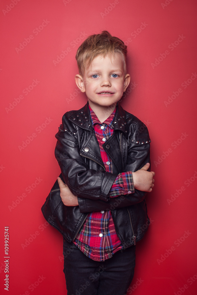 Fashion little boy wearing a leather jacket. Studio portrait over red background Fashion little boy wearing a leather jacket. Studio portrait over red background