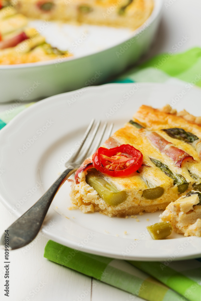 Tart with asparagus and tomatoes on white wooden background.