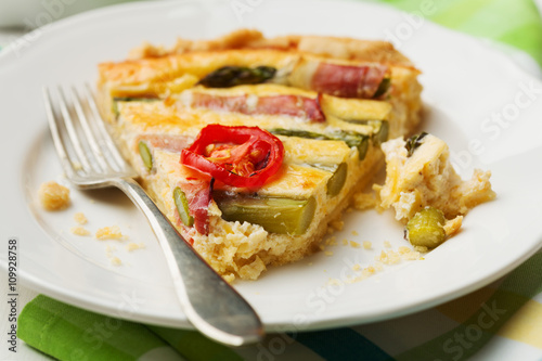 Tart with asparagus and tomatoes on white wooden background.