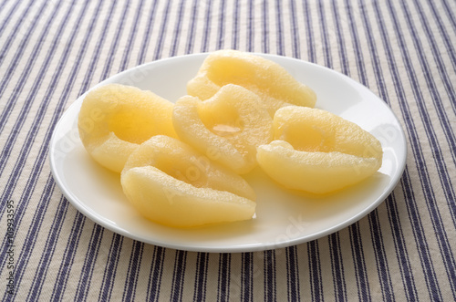 Pears halves on a white plate atop a striped tablecloth side view