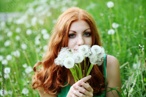 Lifestyle portrait of young spring fashion woman blowing dandelion in spring garden.     © perminoffa