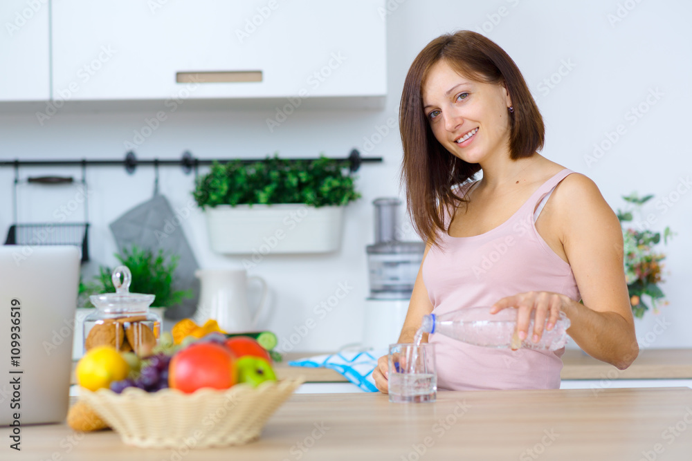 Woman pouring water from a bottle into a glass at the kitchen