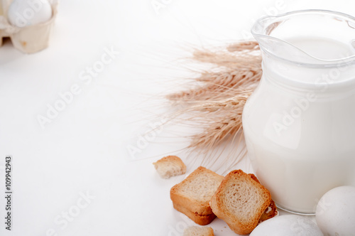 Glass jug with milk, wheat seeds and two eggs