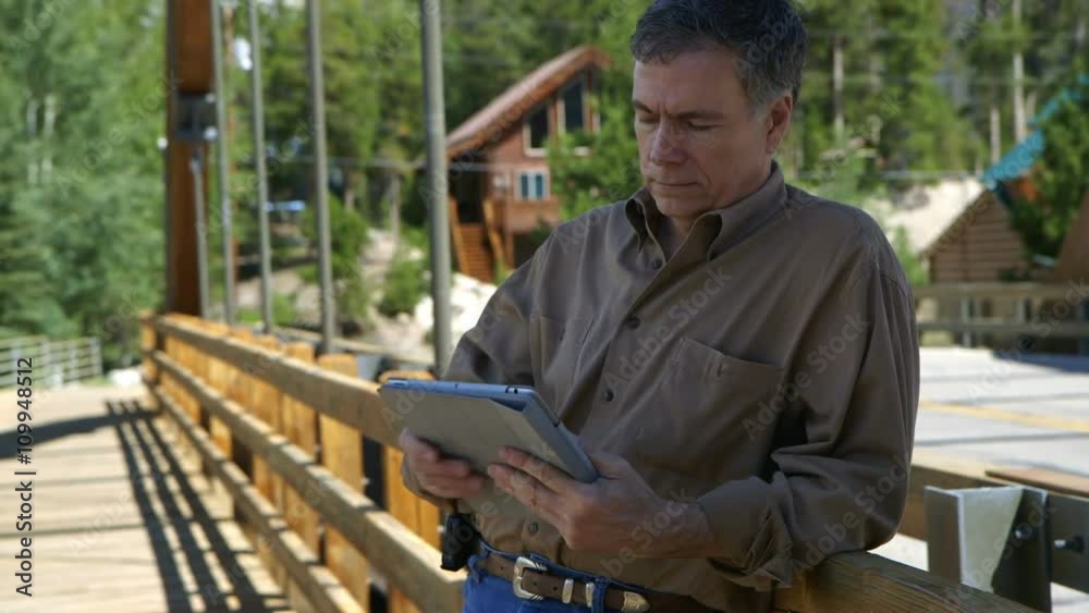 Mature handsome man on the pedestrian walkway of a small bridge stops and uses his digital tablet pc. Mature handsome man on the pedestrian walkway of a small bridge stops and uses his digital tablet pc.